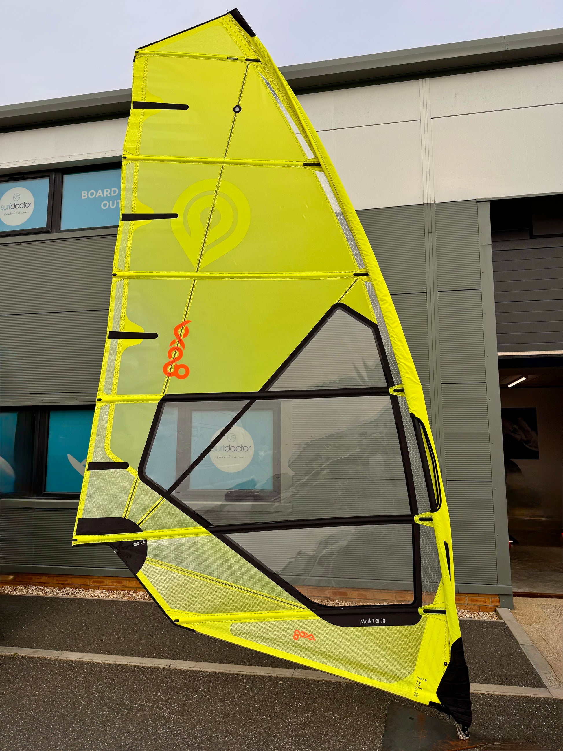 Yellow Goya windsurf sail with Surfdoctor shop branding against a building background