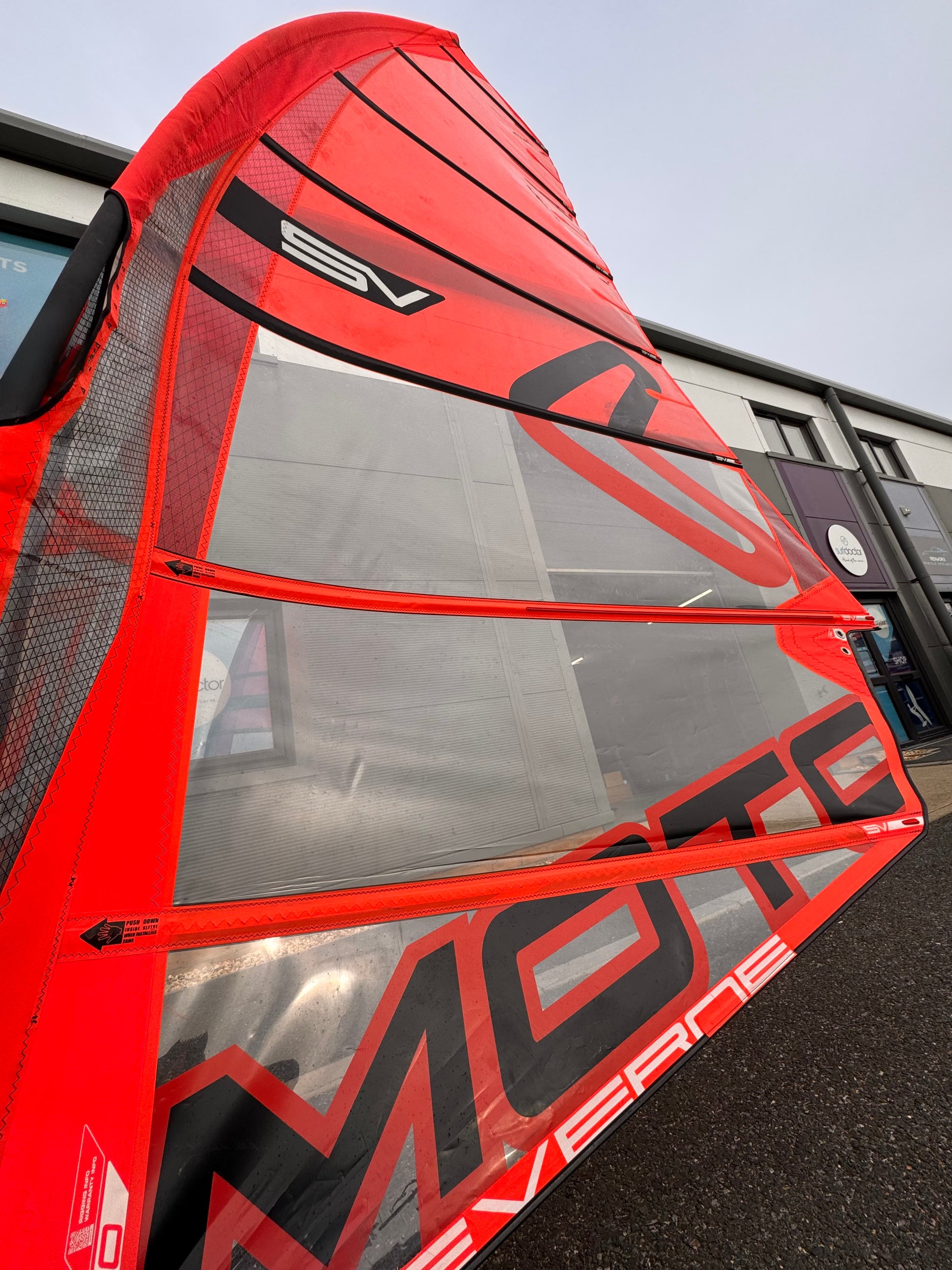 Red and black windsurf sail with Severne Moto in front of Surfdoctor Portland