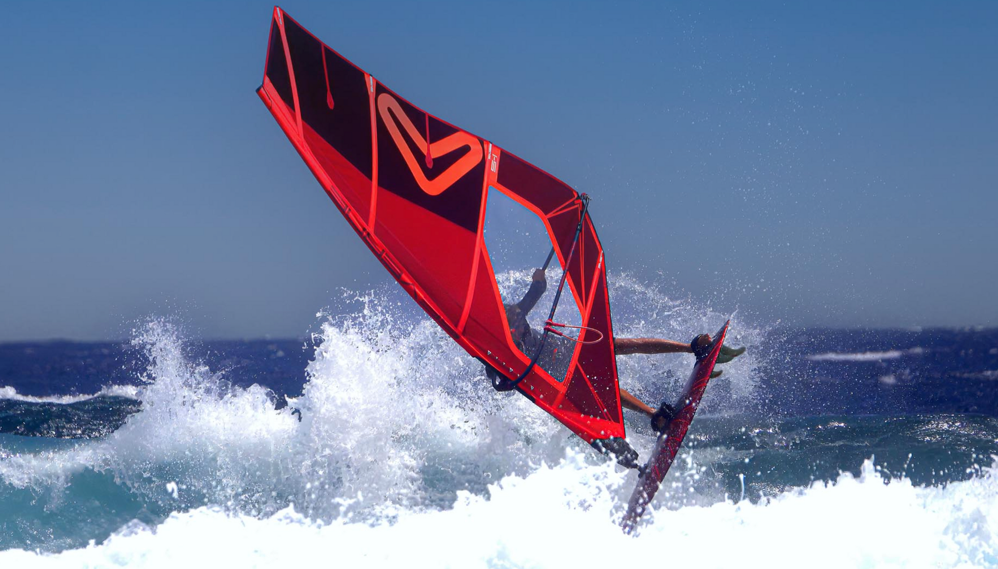 Person windsurfing on a Severne s1 Windsurfing Sail. A red sail against a clear blue sky.