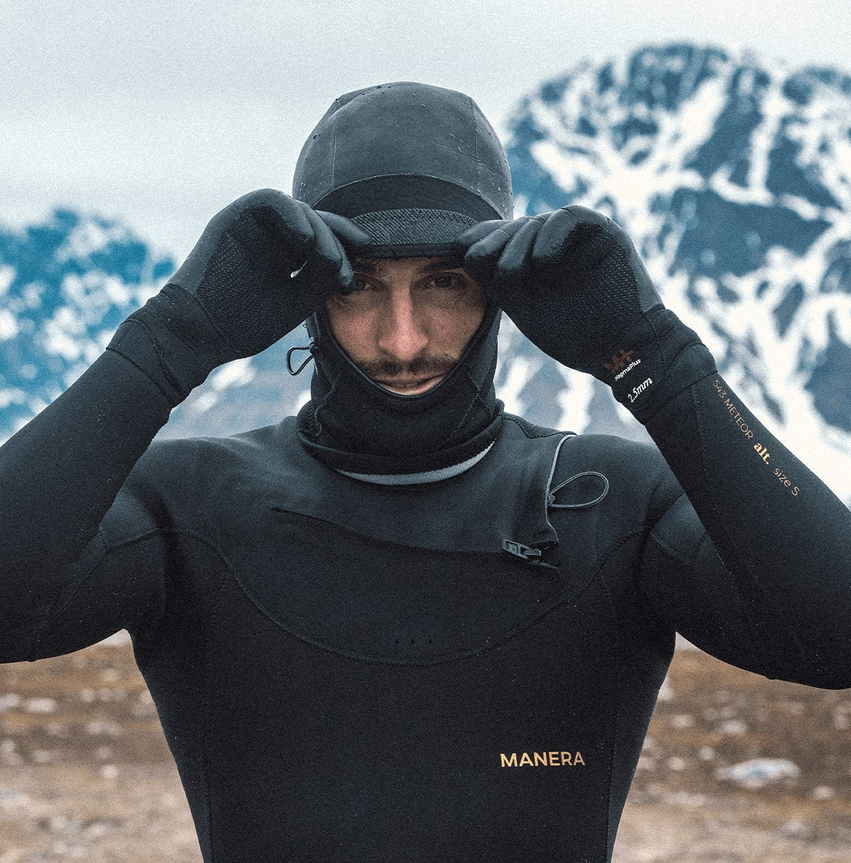 A person wearing a Manera Magama Wetsuit  hood with snowy moutains in the background